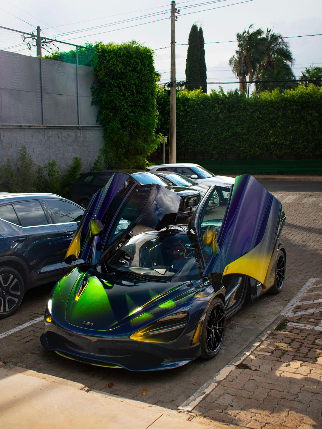 McLaren 750S Coupé com pintura degradê verde, azul, roxo e amarelo, de portas abertas numa rua de Brasília