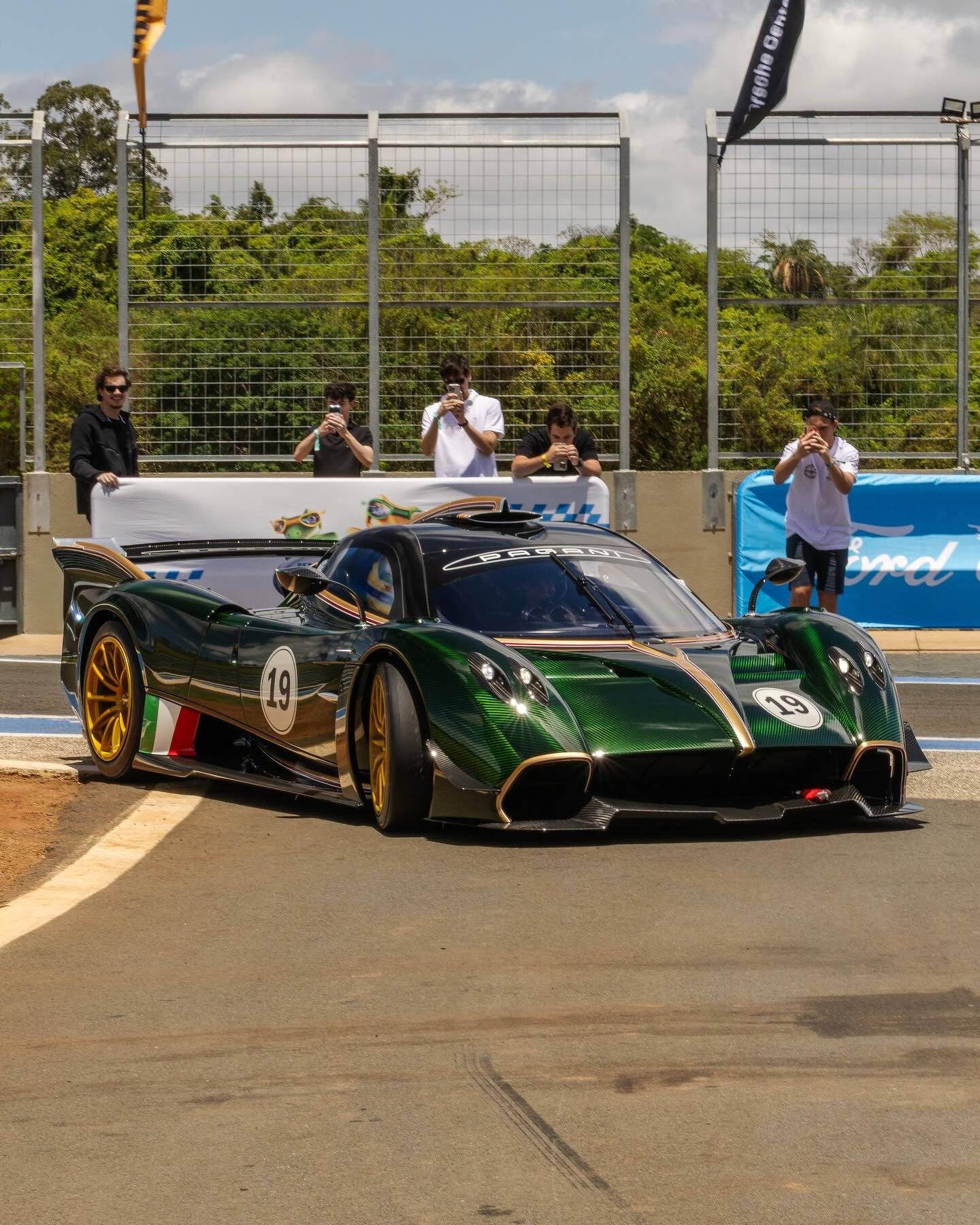 Pagani Huayra R verde com faixa tricolor italiana e o número 19 numa pista em Mogi Guaçu, com espectadores fotografando atrás da grade