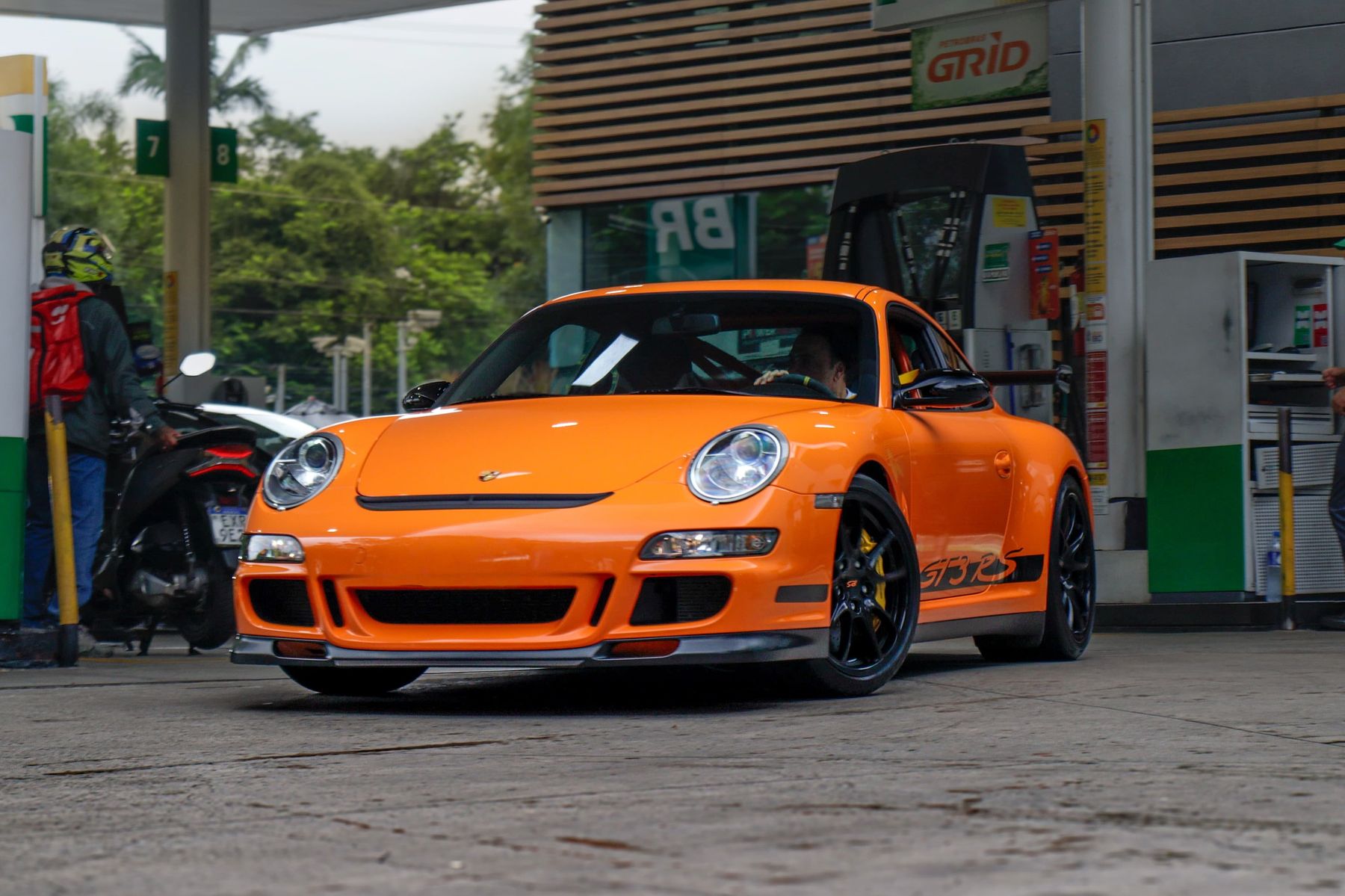 Porsche 911 GT3 RS da geração 997.1 laranja com faixas pretas, estacionado num posto de combustível em São Paulo